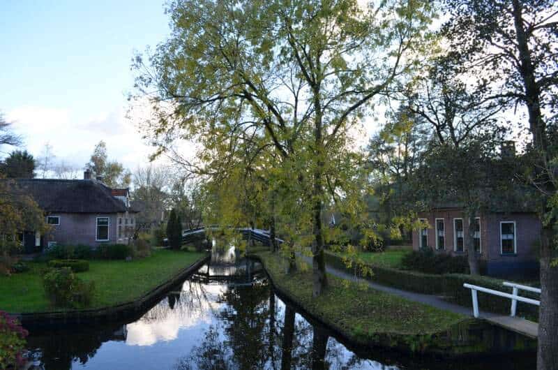 Dorpsgracht van Giethoorn met bruggetjes, bomen in de herfst en karakteristieke rietgedekte boerderijen weerspiegeld in het water.