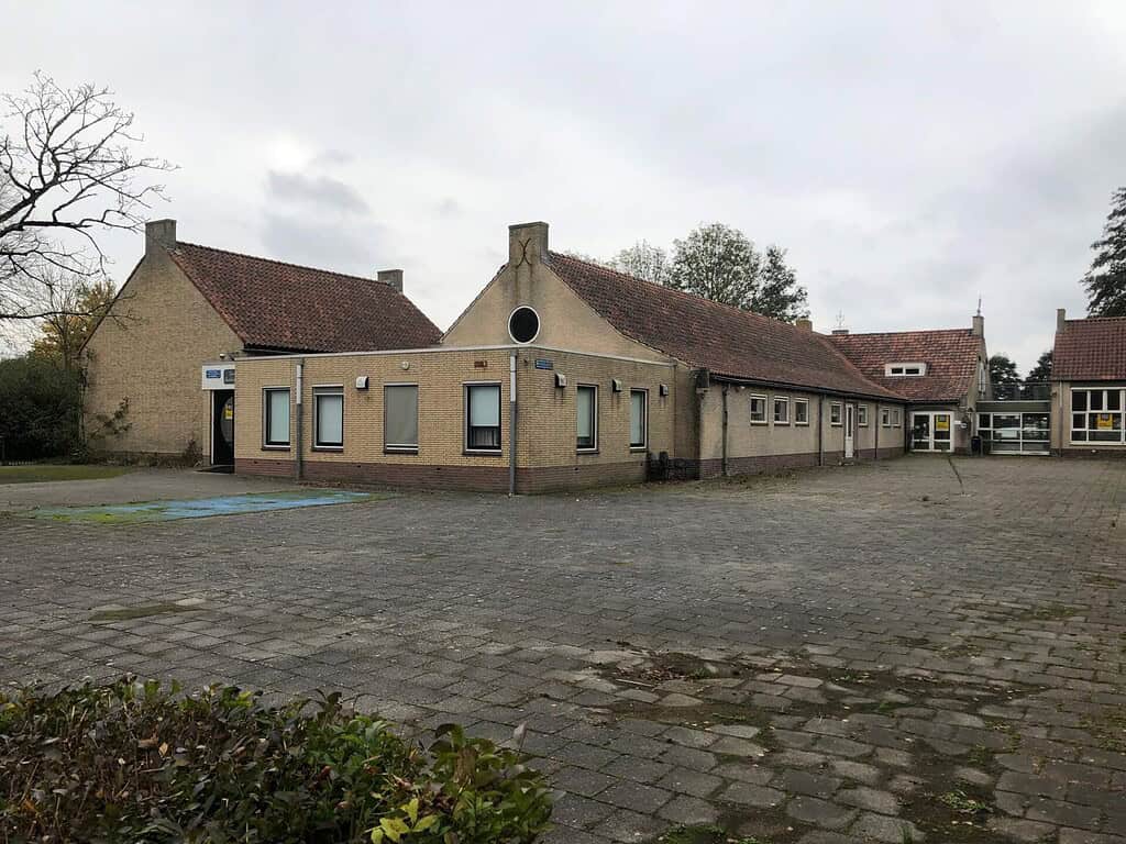 Achterzijde (gevoelsmatig de voorzijde) en schoolplein van de voormalige Zuiderbasisschool, met speelterrein en bakstenen gevels.