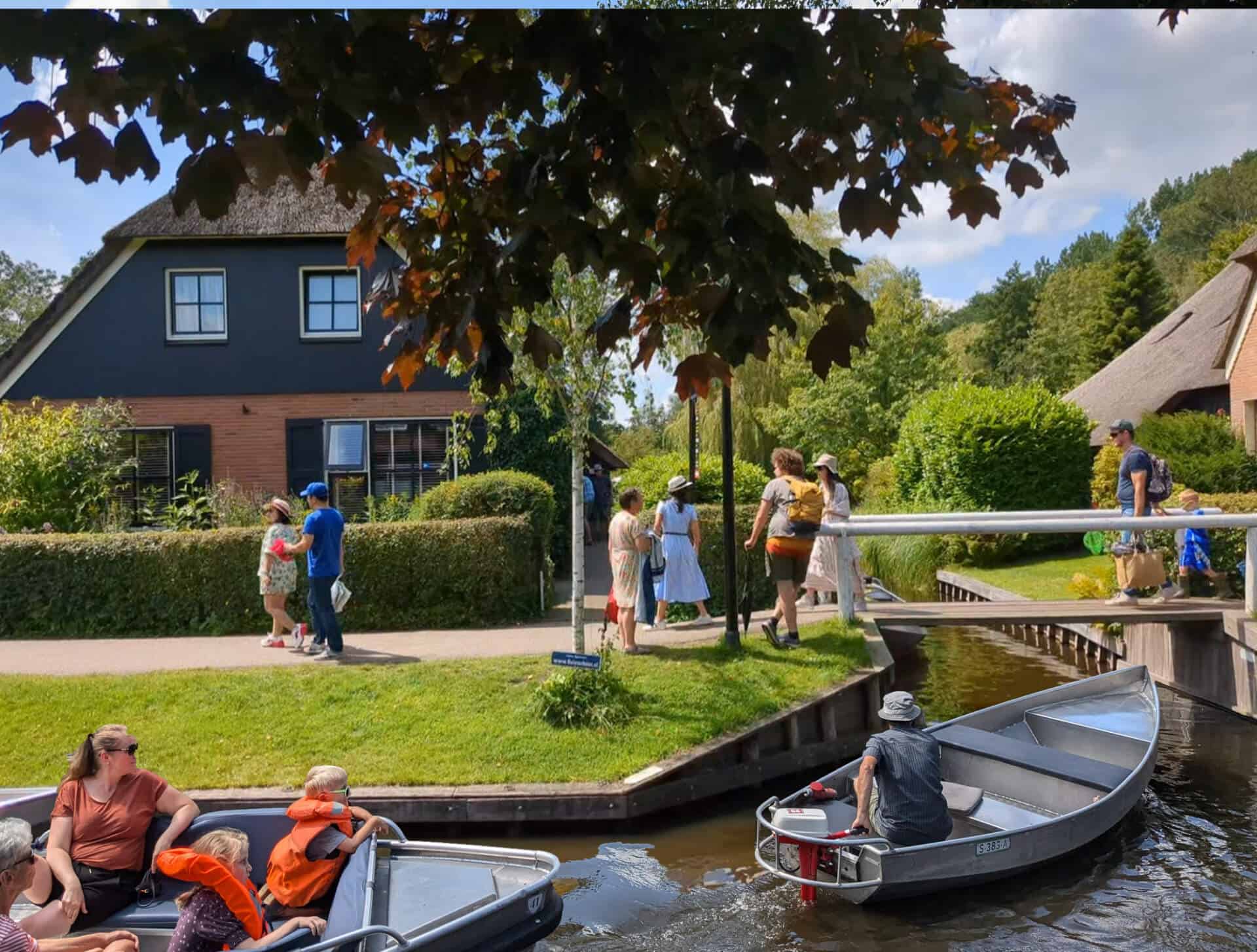 Zomerse gezelligheid langs de Dorpsgracht in Giethoorn Toeristen wandelen langs het Binnenpad terwijl een fluisterboot en een sloep in de dorpsgracht van Giethoorn varen.