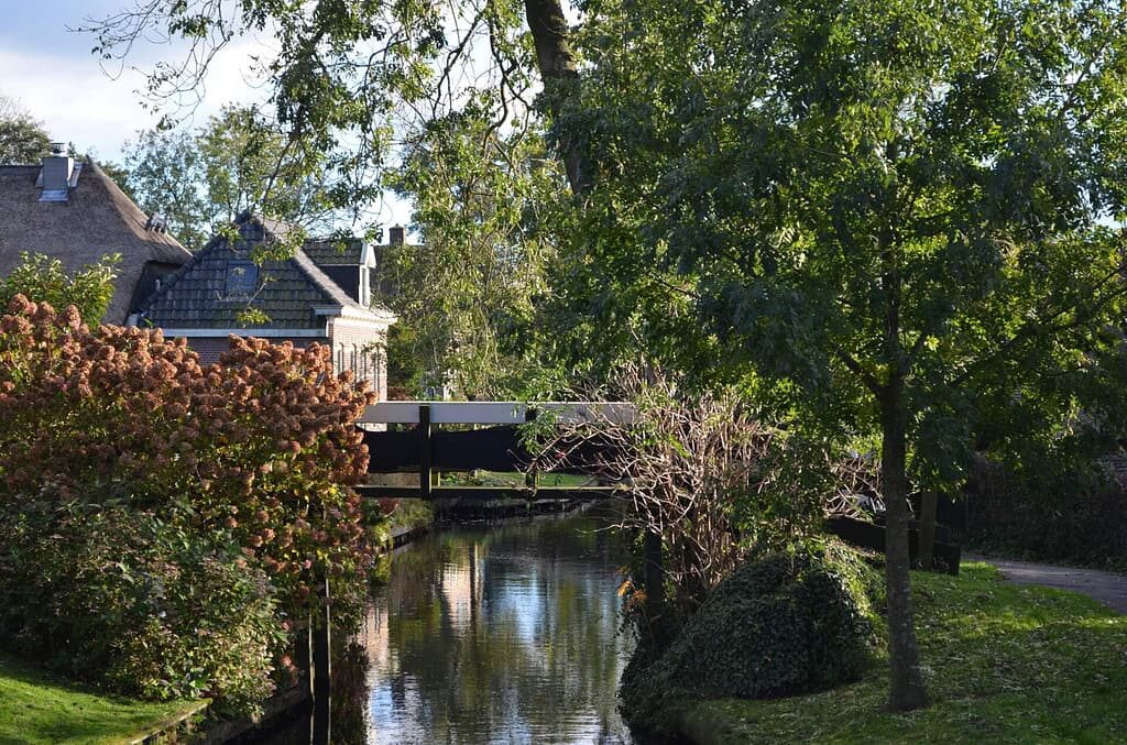 Houten brug over gracht in Giethoorn met eikenhouten schaaldelen, donkere delen en verticale bovenregel op de leuning.